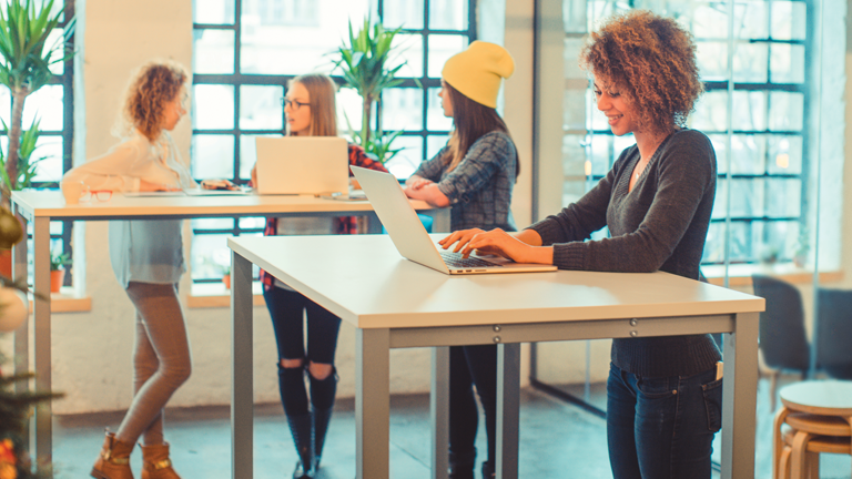 Four women working at standing desks in a modern office