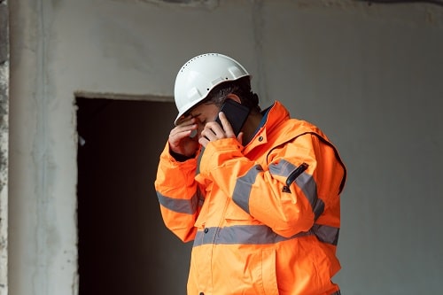 Stressed worker wearing hard hat and orange hi vis jacket on phone