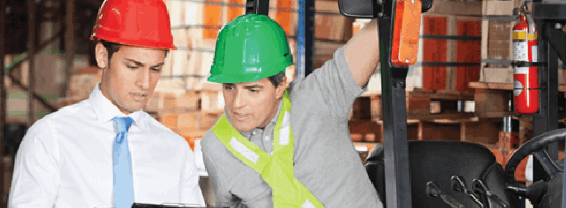 Two people in hard hats at a warehouse looking at a clipboard