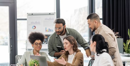 Five people sat around a laptop working together in a modern office