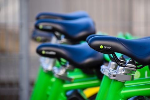 Close-up of several green Lime electric bikes, focusing on the black saddles with the Lime logo, lined up in a row with a blurred background.