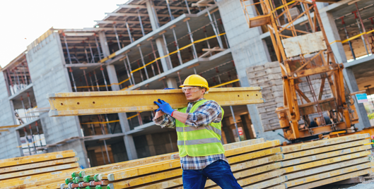 Man on construction site wearing high vis and other PPE carrying steel beam