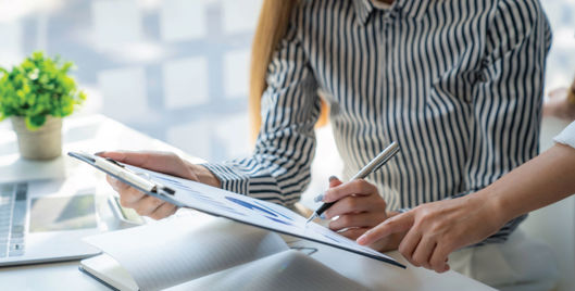 Woman working at desk and looking at a clipboard with colleague