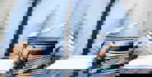 Man in business attire writing notes with a binder on the desk in front of him