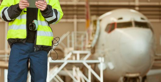 Man wearing high vis and holding an ipad standing in front of a plane in a hangar