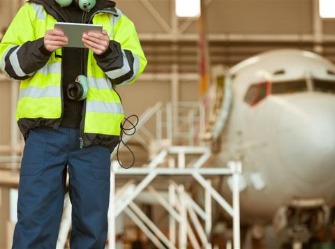 Man wearing high vis and holding an ipad standing in front of a plane in a hangar